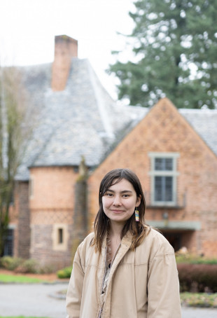 Elise posing in front of the Manor House, wearing a tan jacket.