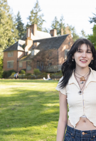 Grayson smiling outside the Manor House on the undergrad campus. She is wearing a white top and blue jeans.